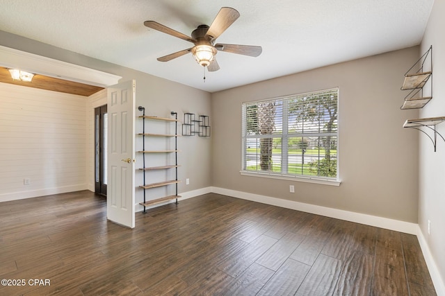 unfurnished room featuring dark wood-style floors, a ceiling fan, and baseboards