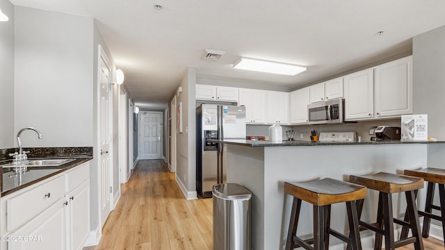 kitchen featuring visible vents, a breakfast bar, a peninsula, a sink, and stainless steel appliances