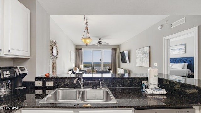 kitchen featuring visible vents, a ceiling fan, a sink, open floor plan, and white cabinetry