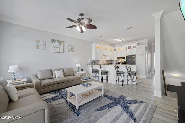 living area featuring visible vents, ornamental molding, a ceiling fan, light wood-style floors, and baseboards