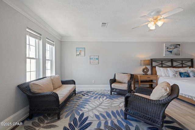 bedroom featuring wood finished floors, visible vents, baseboards, a textured ceiling, and crown molding