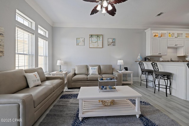 living area featuring light wood finished floors, visible vents, a ceiling fan, and ornamental molding