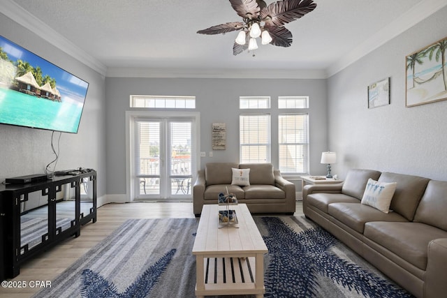 living room featuring crown molding, baseboards, light wood finished floors, and ceiling fan