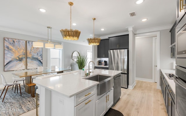 kitchen with crown molding, a kitchen island with sink, stainless steel appliances, and a sink