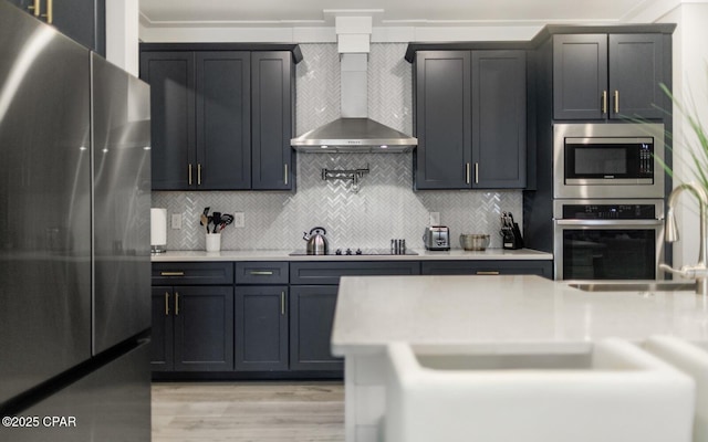 kitchen with decorative backsplash, light wood-style flooring, wall chimney exhaust hood, stainless steel appliances, and light countertops