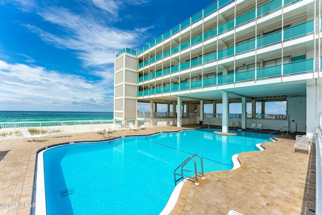 pool with a patio, a water view, and a view of the beach