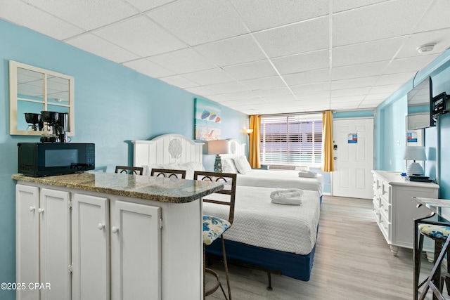 bedroom featuring a drop ceiling and light wood-style floors