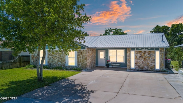 view of front of home with stone siding, metal roof, fence, and a front lawn