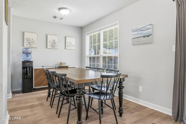 dining room with a textured ceiling, light wood-type flooring, visible vents, and baseboards