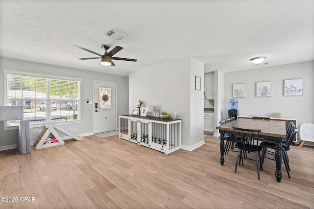 dining space with light wood finished floors, visible vents, a ceiling fan, a textured ceiling, and baseboards