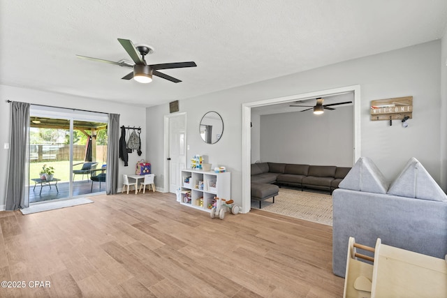 living area featuring light wood finished floors, a ceiling fan, and a textured ceiling