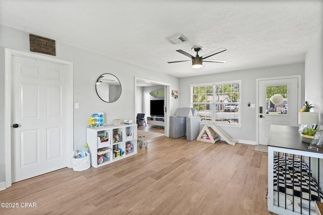 playroom with a textured ceiling, ceiling fan, wood finished floors, visible vents, and baseboards