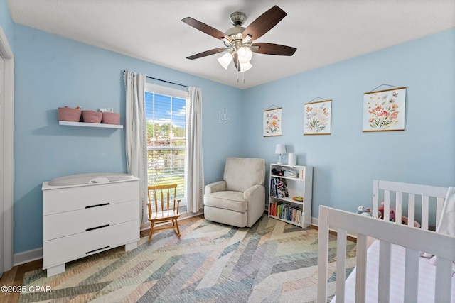 bedroom with a nursery area, ceiling fan, baseboards, and wood finished floors