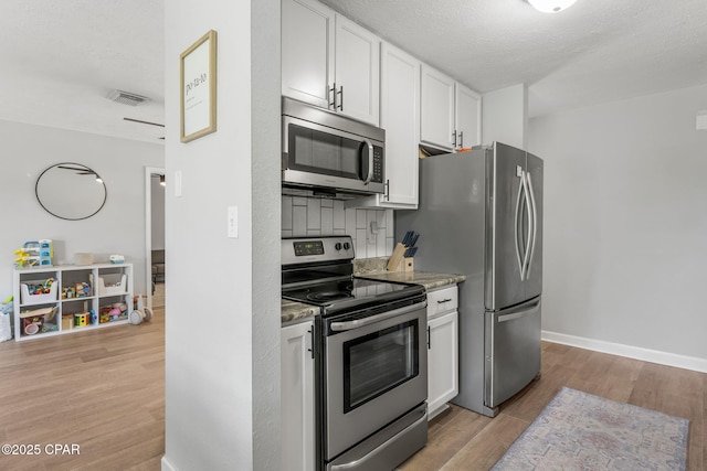 kitchen featuring stainless steel appliances, visible vents, baseboards, white cabinetry, and light wood-style floors