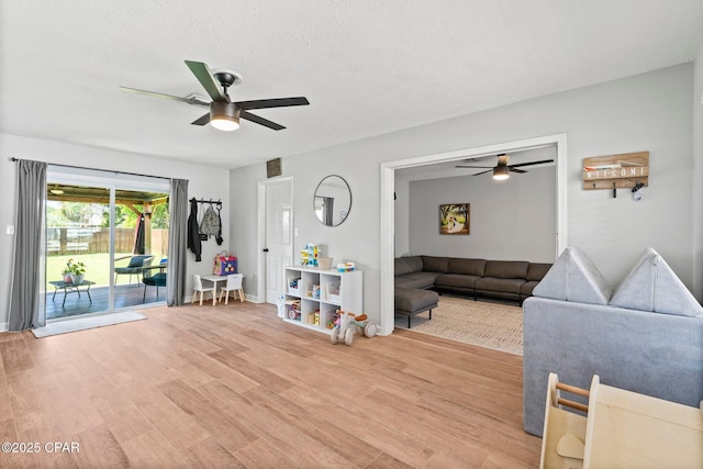 living area featuring light wood-style floors, a ceiling fan, and a textured ceiling