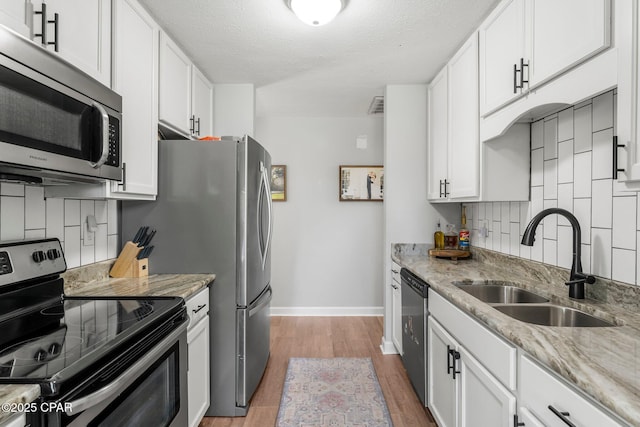 kitchen with appliances with stainless steel finishes, white cabinets, a sink, and decorative backsplash