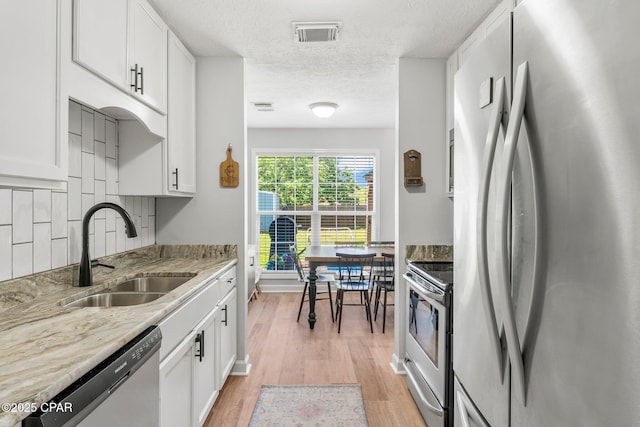 kitchen with visible vents, appliances with stainless steel finishes, light wood-style floors, white cabinetry, and a sink