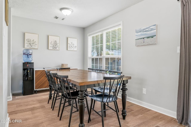 dining area with a textured ceiling, light wood finished floors, visible vents, and baseboards