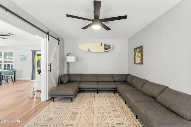 living area with ceiling fan, a barn door, light wood-style flooring, and baseboards