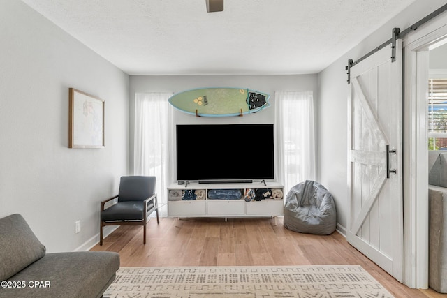 sitting room featuring a textured ceiling, a barn door, wood finished floors, and baseboards