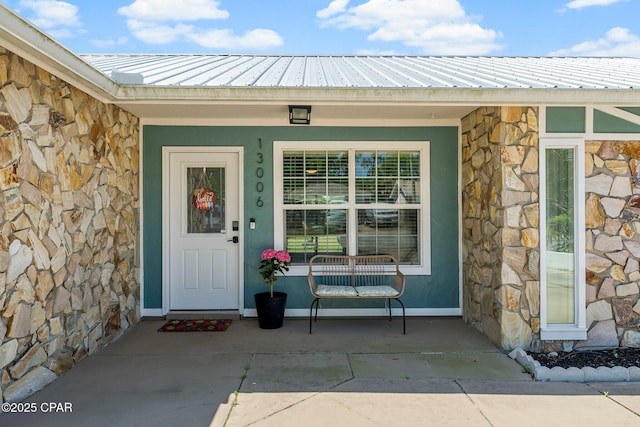 property entrance with stone siding, covered porch, and metal roof