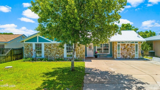 view of front facade with driveway, stone siding, metal roof, fence, and a front yard