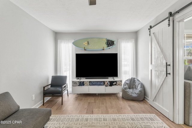 living area featuring a barn door, a textured ceiling, baseboards, and wood finished floors