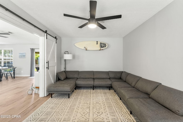 living area with light wood finished floors, a barn door, a ceiling fan, and baseboards