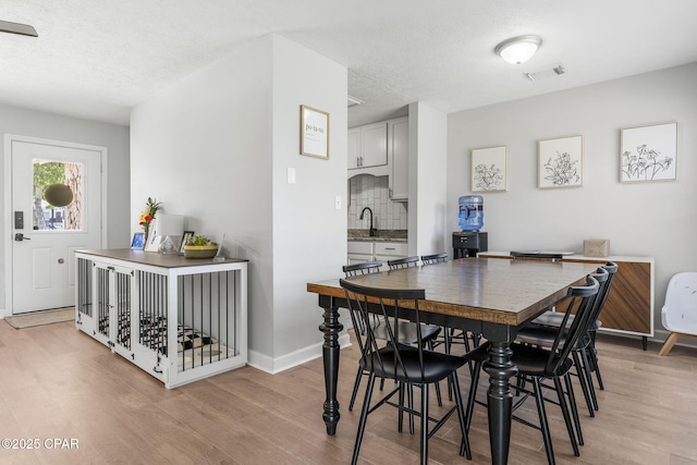 dining area with baseboards, a textured ceiling, visible vents, and light wood-style floors