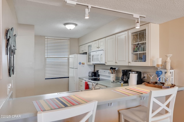 kitchen with a kitchen bar, a textured ceiling, white appliances, light countertops, and glass insert cabinets