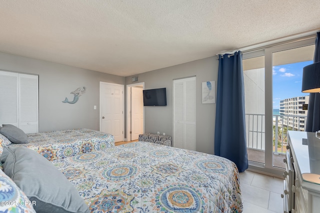 bedroom featuring expansive windows, a textured ceiling, light tile patterned flooring, and access to outside