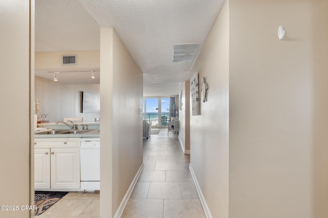 hallway with a textured ceiling, light tile patterned floors, visible vents, and a sink