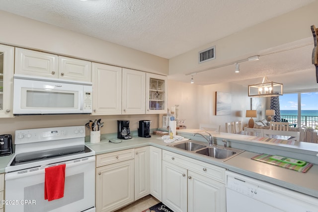 kitchen featuring white appliances, visible vents, a sink, glass insert cabinets, and a textured ceiling