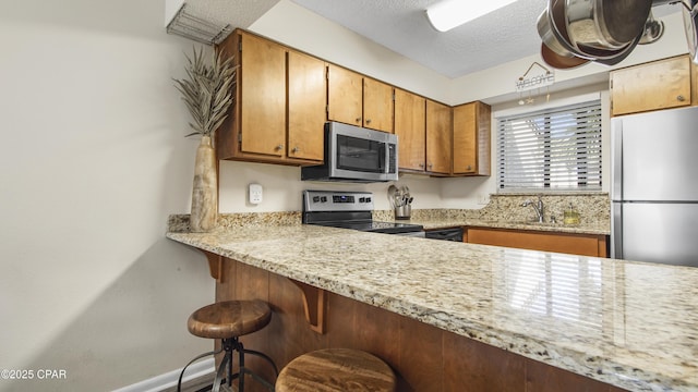 kitchen with a breakfast bar area, stainless steel appliances, brown cabinetry, a textured ceiling, and a sink