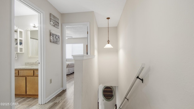 hall featuring a sink, light wood-type flooring, an upstairs landing, and baseboards