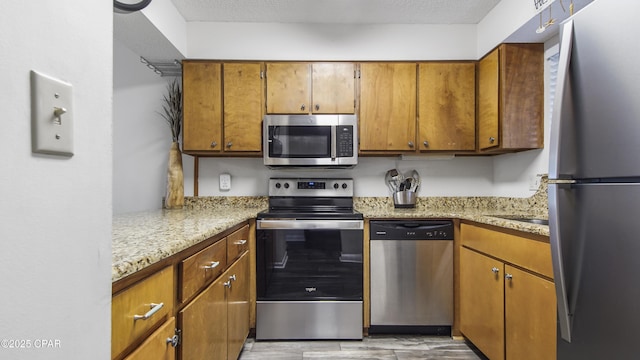 kitchen featuring light stone countertops, brown cabinets, appliances with stainless steel finishes, and a textured ceiling