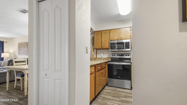 kitchen with a textured ceiling, wood finish floors, visible vents, and stainless steel appliances