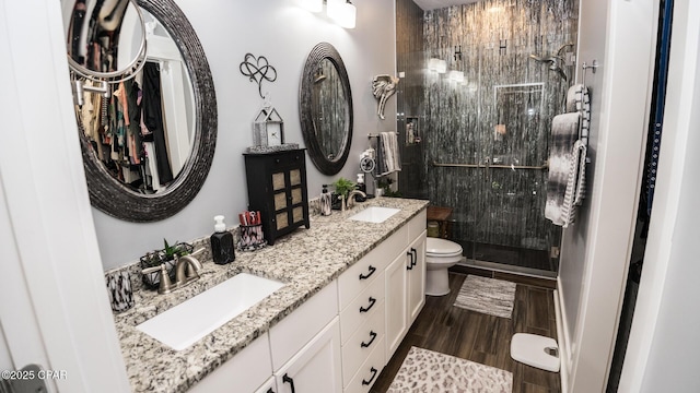 full bath featuring wood finish floors, toilet, double vanity, a stall shower, and a sink