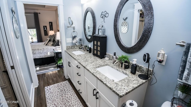 ensuite bathroom with double vanity, connected bathroom, wood finished floors, and a sink