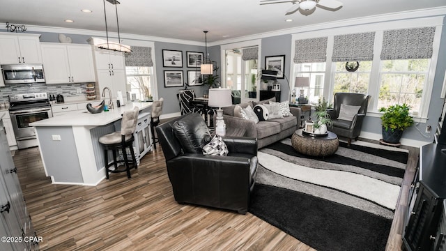 living room with ceiling fan, crown molding, baseboards, and wood finished floors