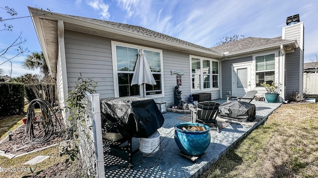 back of house featuring a patio area, a chimney, roof with shingles, and an outdoor fire pit