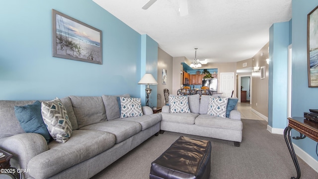 carpeted living room featuring ceiling fan with notable chandelier and baseboards