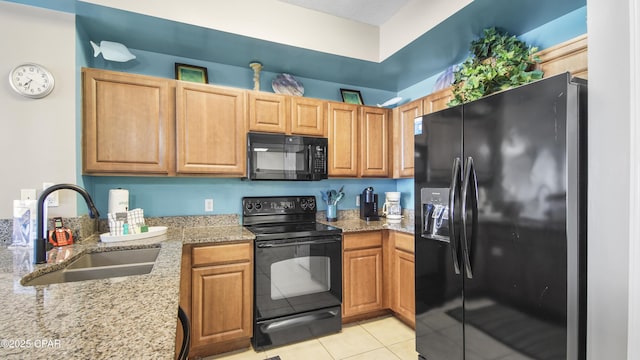 kitchen with light tile patterned flooring, light stone countertops, black appliances, and a sink