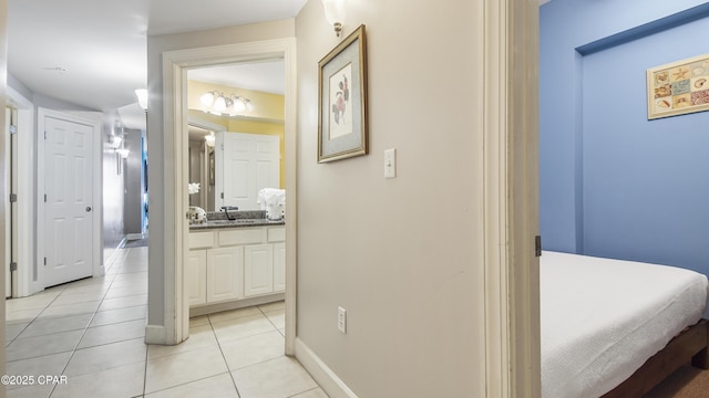 corridor with light tile patterned floors, baseboards, and a sink