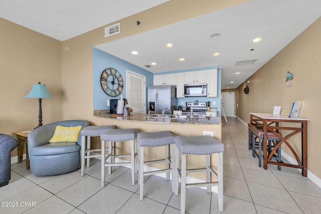 kitchen featuring stainless steel appliances, a peninsula, visible vents, a kitchen breakfast bar, and white cabinetry