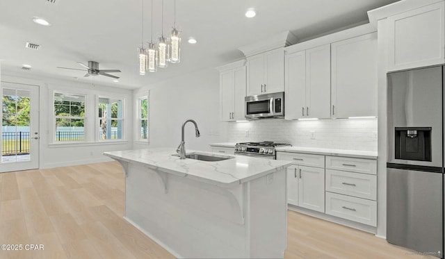 kitchen featuring light stone countertops, a center island with sink, a sink, decorative backsplash, and stainless steel appliances