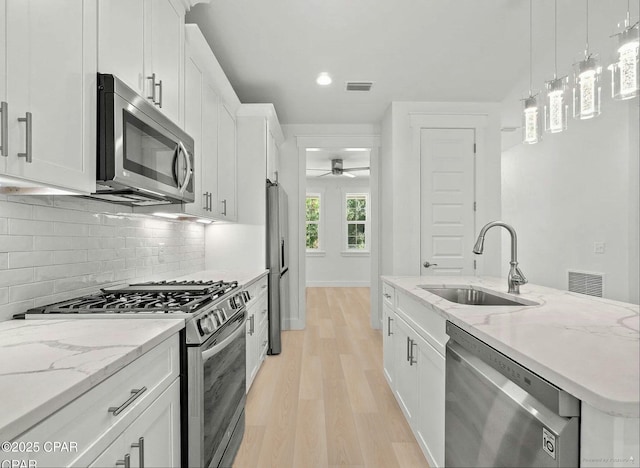 kitchen featuring backsplash, light wood-style flooring, white cabinets, stainless steel appliances, and a sink