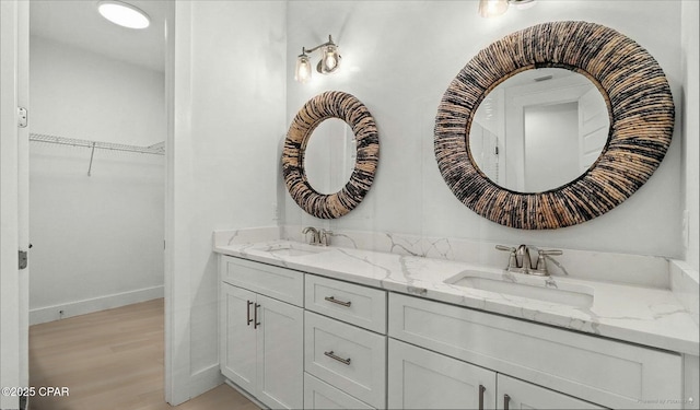 bathroom featuring double vanity, a spacious closet, baseboards, and a sink