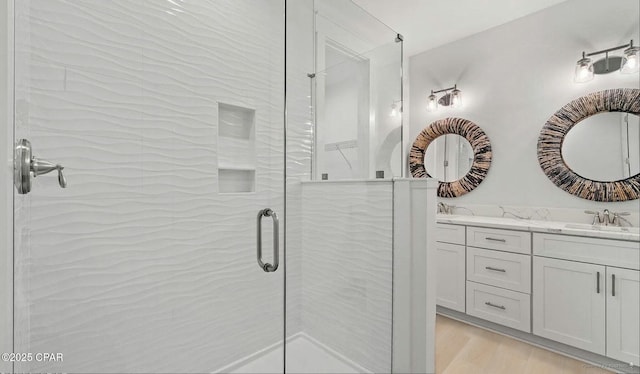 bathroom featuring a shower stall, wood finished floors, double vanity, and a sink