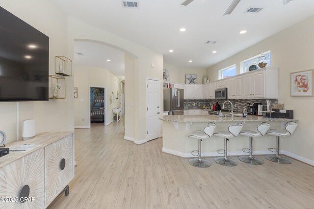 kitchen with visible vents, arched walkways, light wood-style floors, appliances with stainless steel finishes, and a peninsula